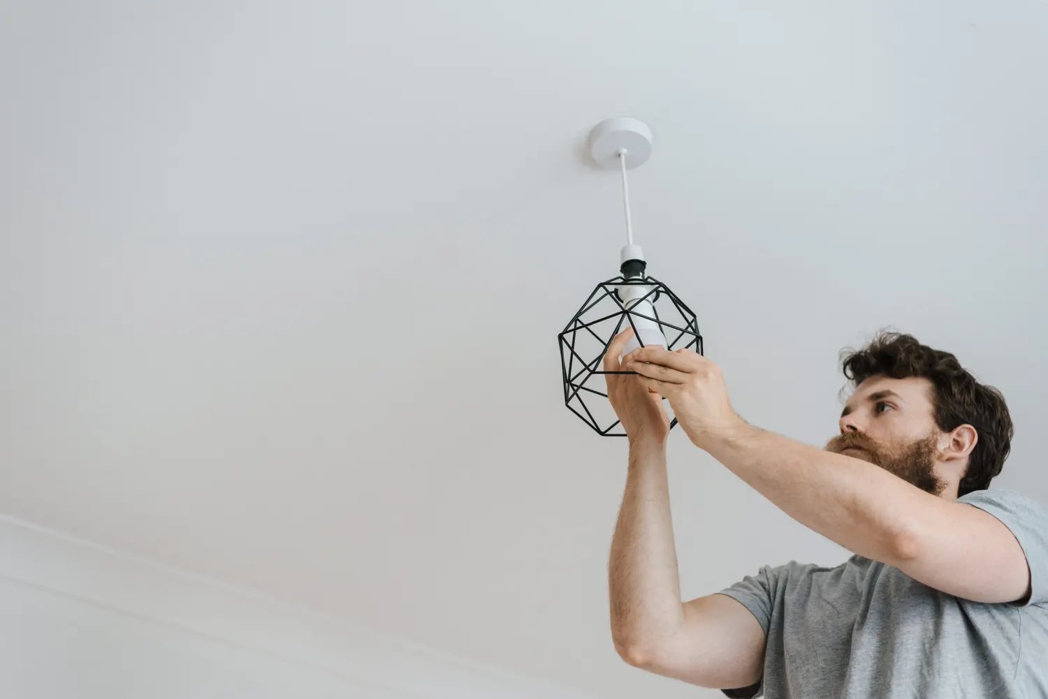 Elektriker monterer en moderne taklampe i en leilighet